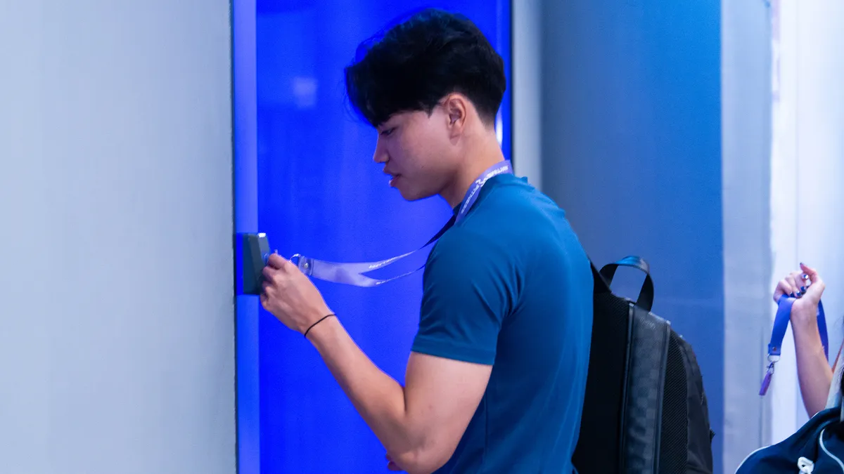 Young man with backpack scanning a card on a device mounted on a blue wall.