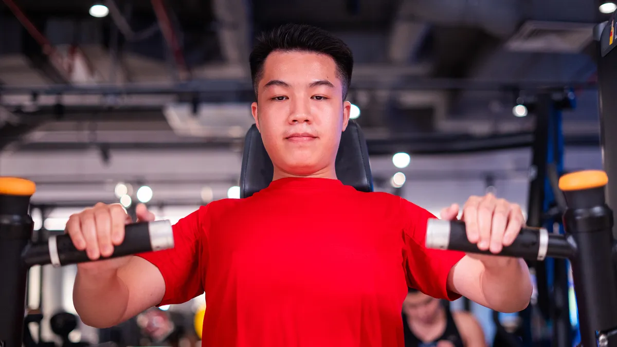Nam thanh niên mặc áo đỏ đang sử dụng máy tập trong phòng tập để rèn luyện sức mạnh trong nhà.