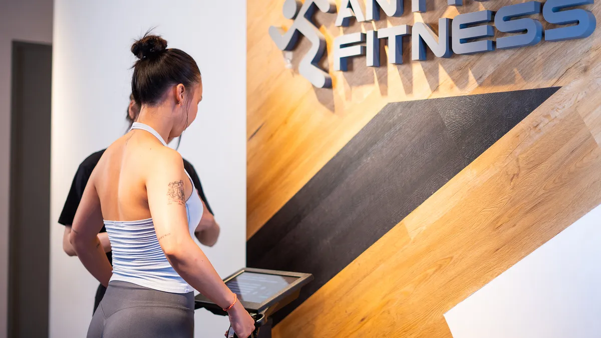 Người phụ nữ mặc đồ tập đang kiểm tra một máy tập trước biển hiệu Anytime Fitness.