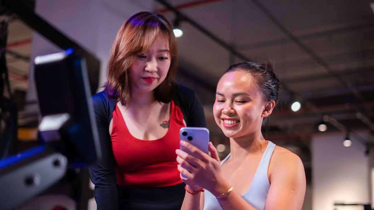 Hai phụ nữ trẻ mặc đồ tập đang nhìn vào điện thoại thông minh trong khung cảnh phòng tập.