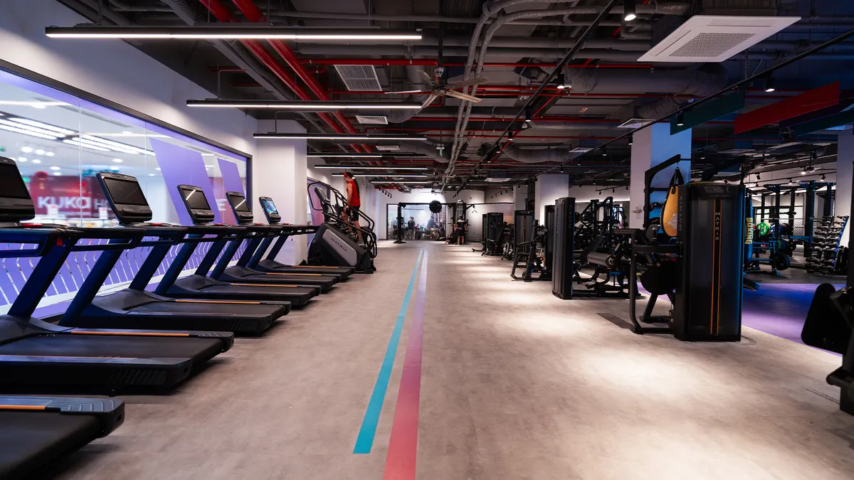 Modern gym interior with treadmills on the left and weight machines on the right under exposed ceilings.