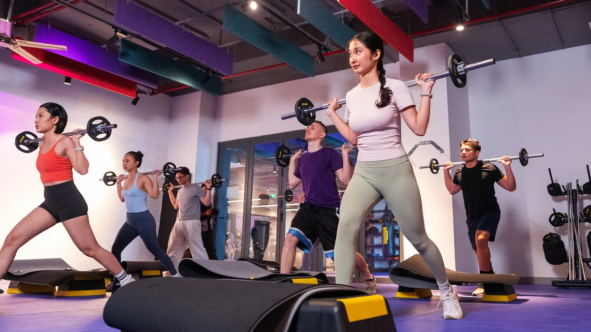 Group of people lifting barbells and doing lunges in a gym workout class.