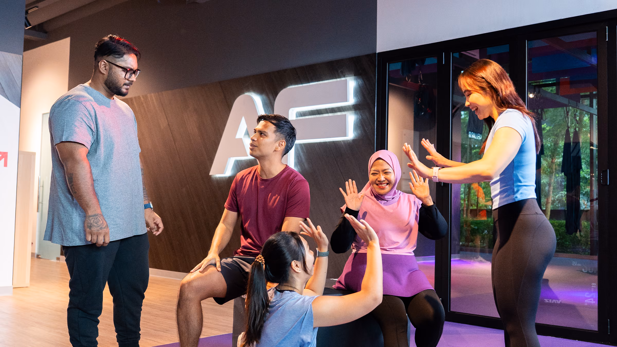 Group of five diverse adults socializing and exercising together in a modern gym setting.