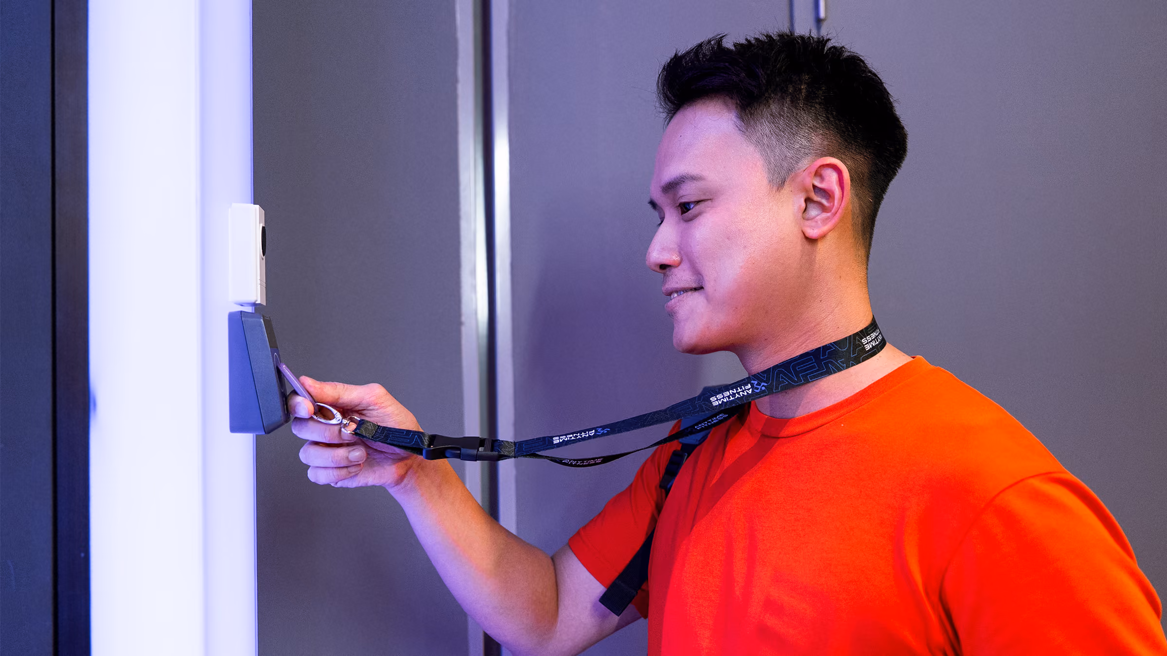 Man in orange shirt holding lanyard to scan an access card at a wall scanner.