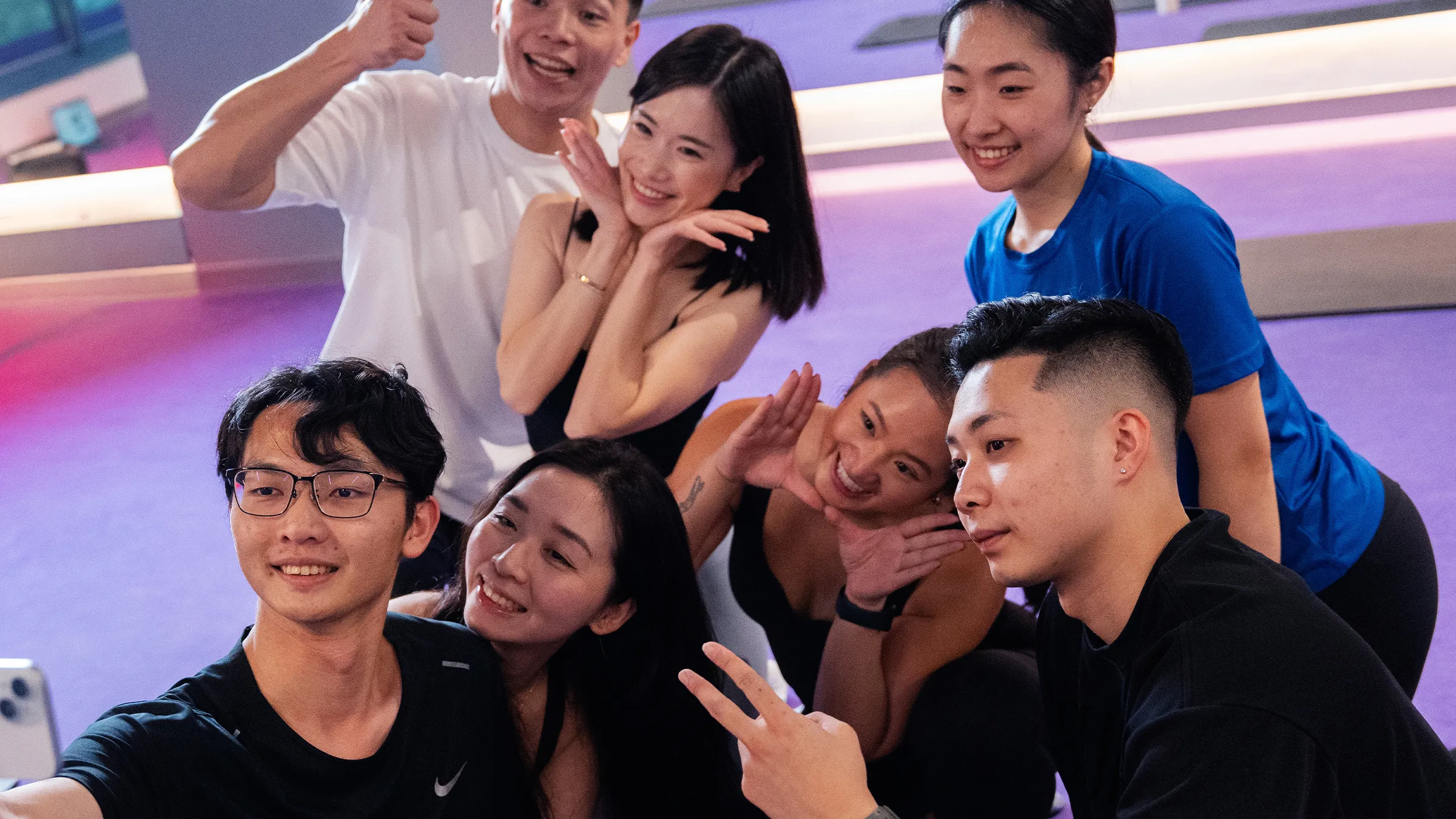 六位年輕人在擁有紫色地板的室內健身房拍照和微笑自拍。