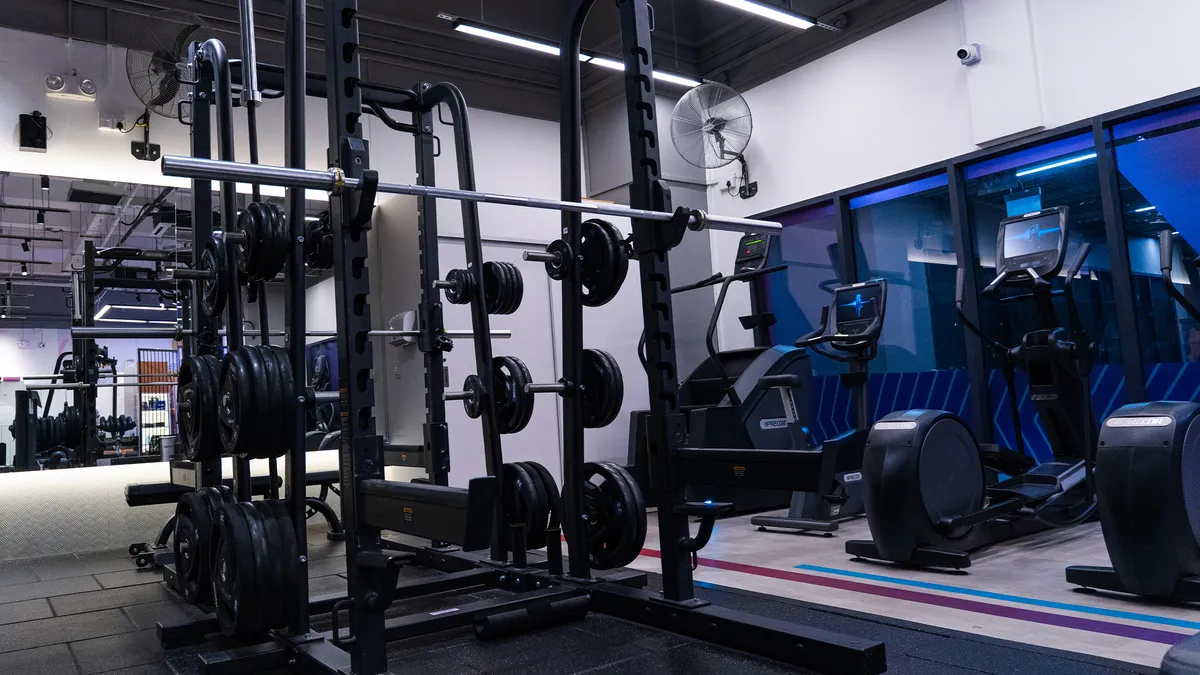 Gym with weightlifting rack, barbell with plates, exercise bikes, and mirrors on the wall.