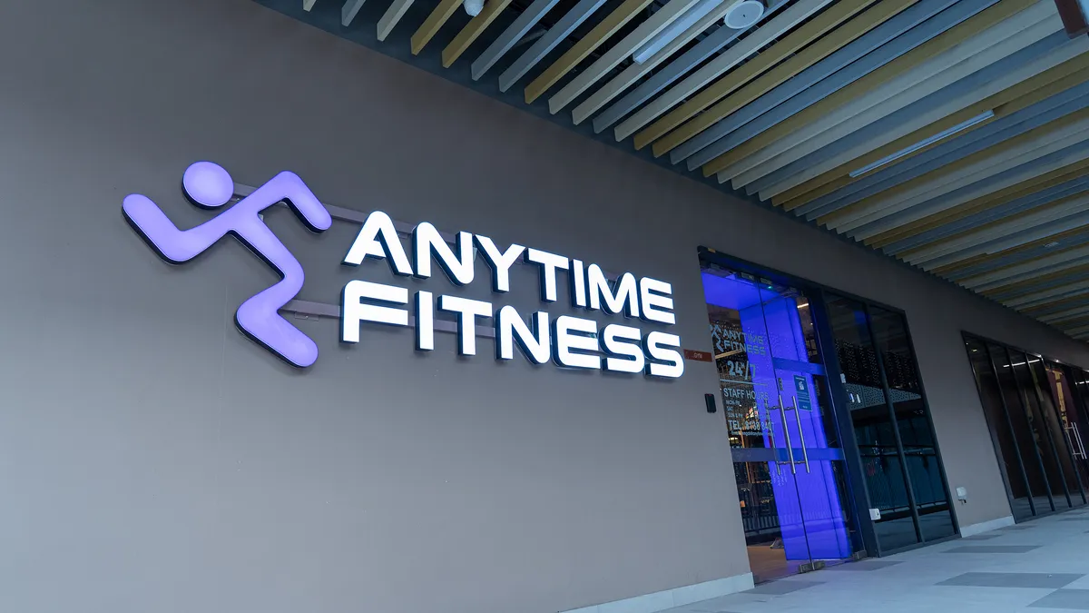 Exterior of Anytime Fitness gym with a glowing purple running figure logo and white text on gray wall.