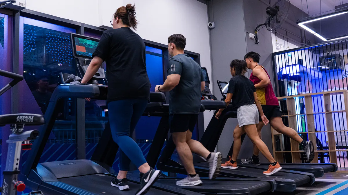Four people exercising on treadmills side by side in a modern gym setting.