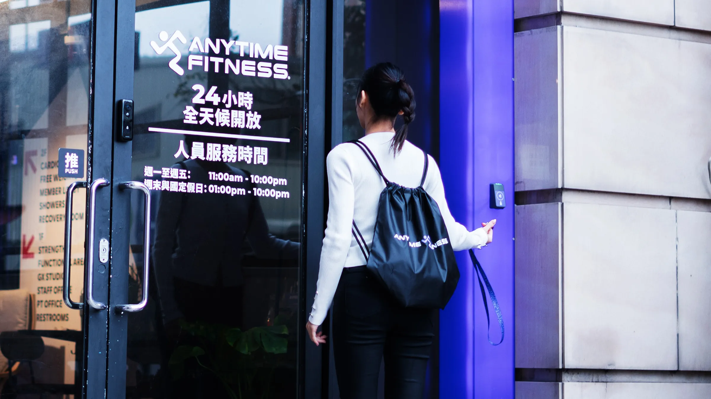 戴著黑色袋子的女人按 Anytime Fitness 健身房門口旁邊的門禁板。