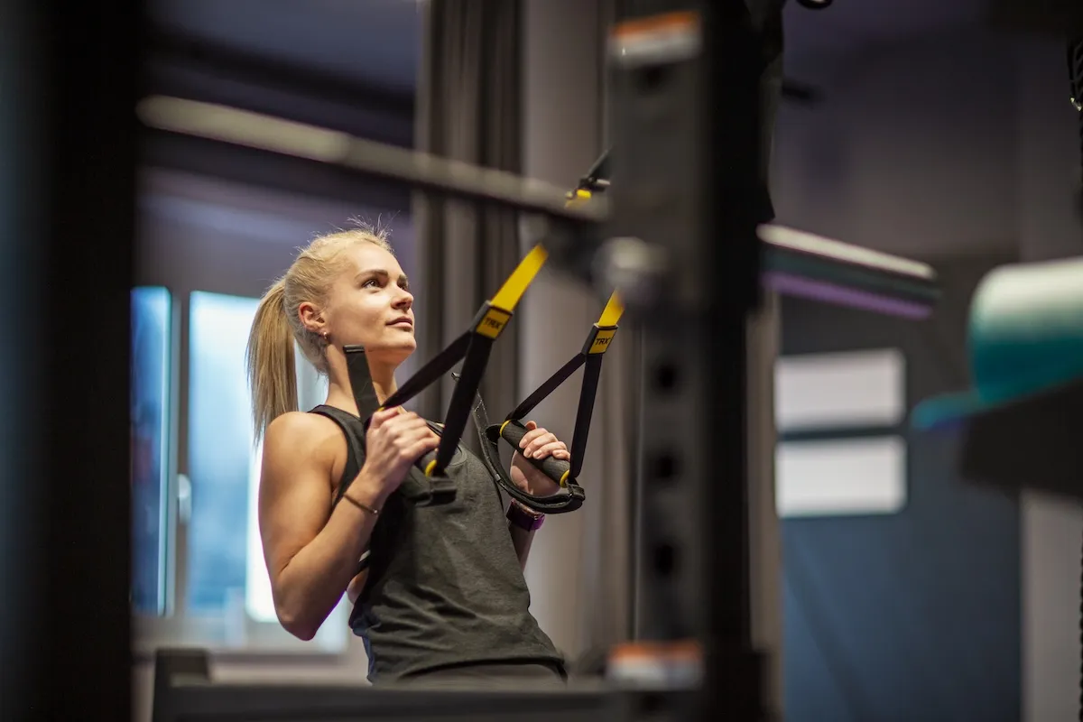 Eine junge Frau absolviert ein Oberkörpertraining mit einem Schlingentrainer (TRX) im Gym.