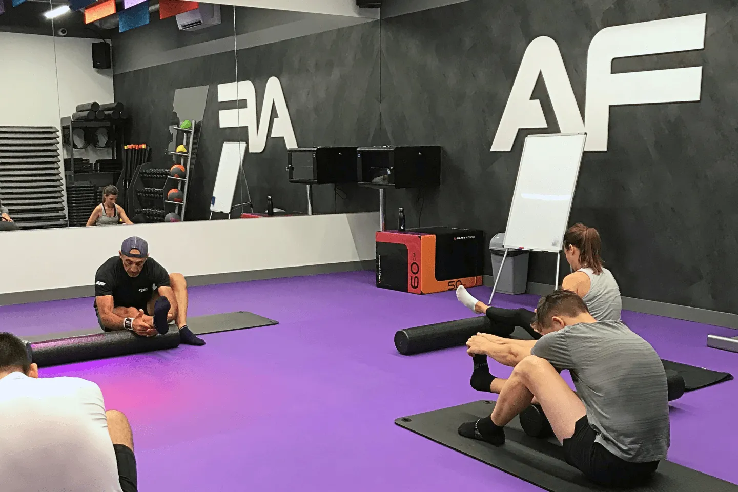 Séance d'étirements et de récupération en groupe avec rouleaux de massage dans la salle d'entraînement Anytime Fitness.