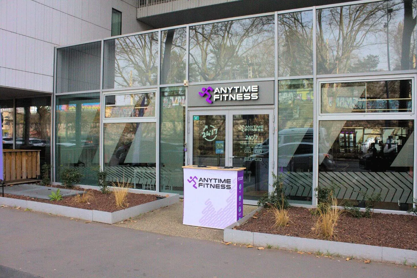 Façade vitrée de la salle de sport Anytime Fitness 24/7 avec comptoir d'accueil devant l'entrée.