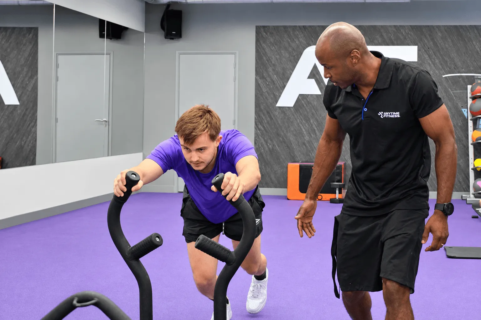 Un homme effectuant un exercice de gainage sous la supervision d'un coach Anytime Fitness.