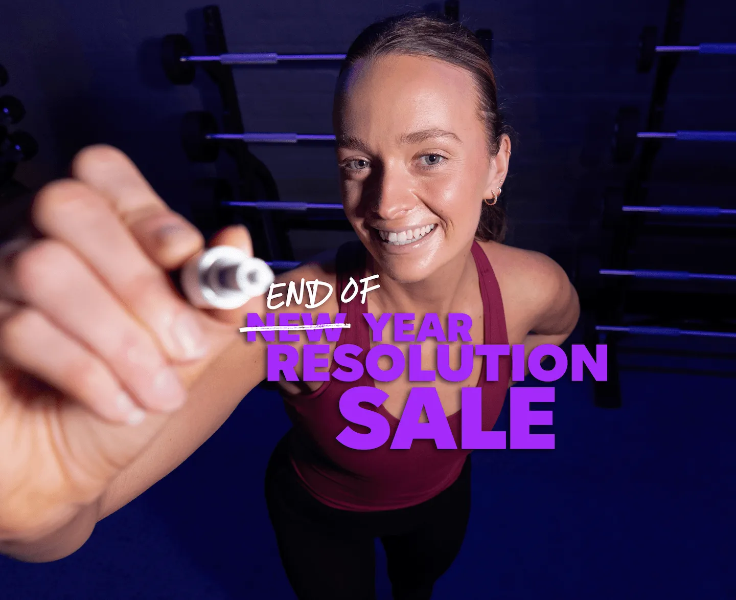 Smiling woman holding a marker in a gym with “End of Year Resolution Sale” promotional text.