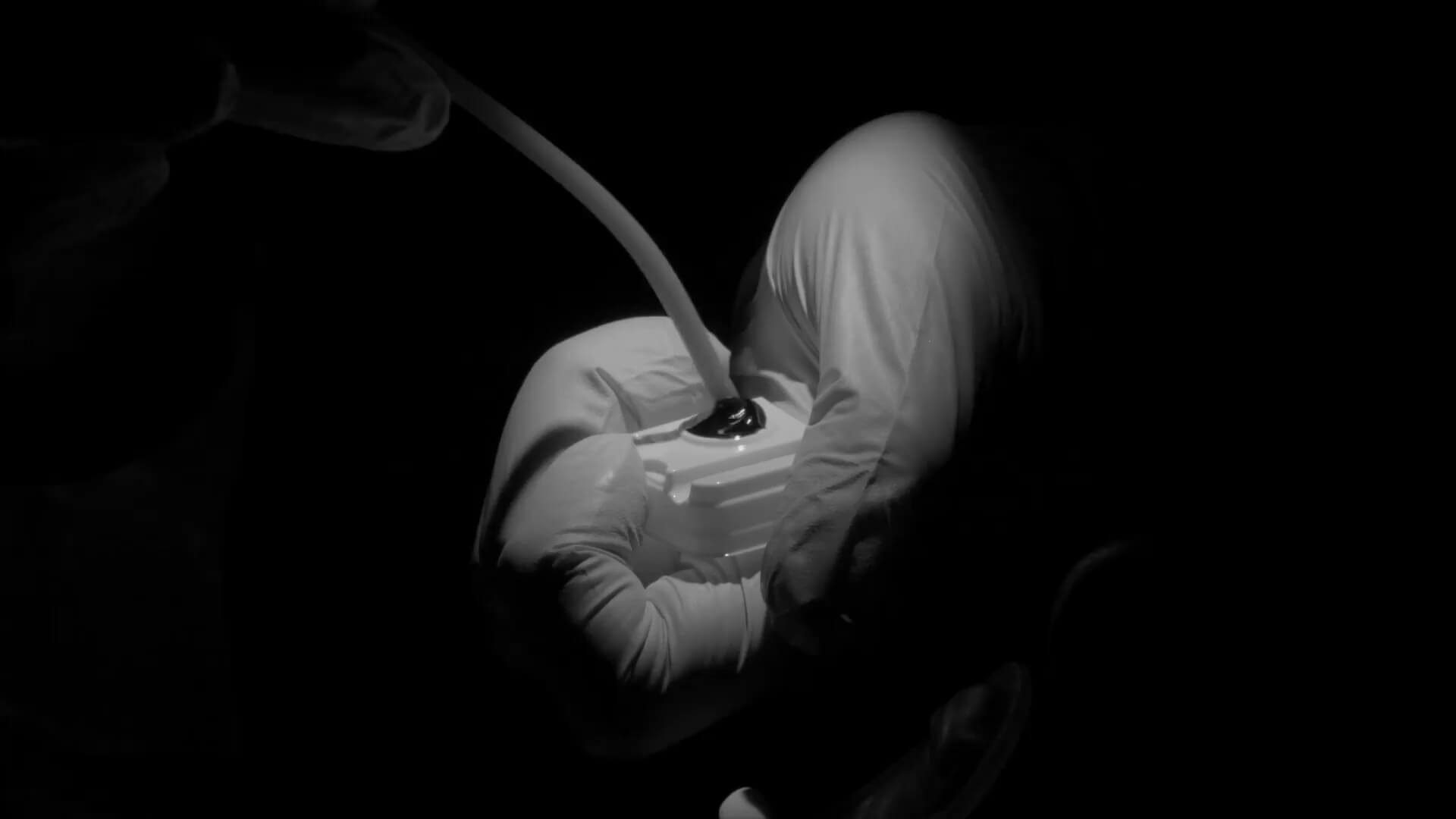 Gloved hand holding a small device with a tube inserted under focused lighting on a black background.