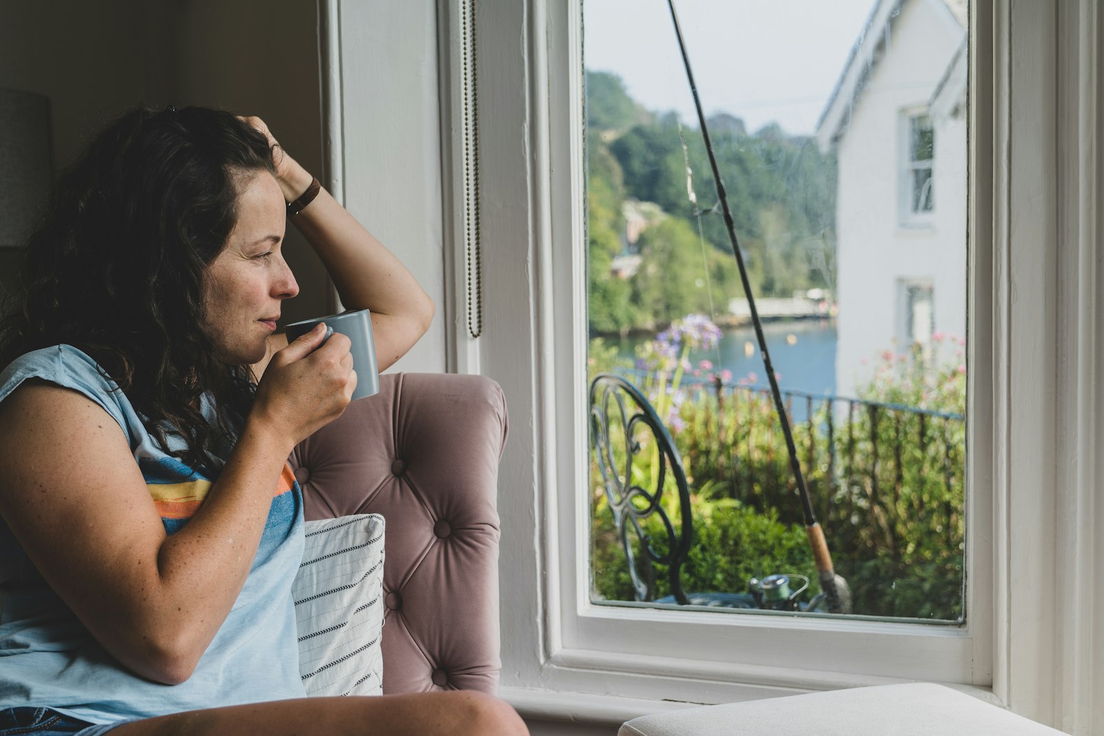 Thoughtful woman with a cup of tea by a window at home