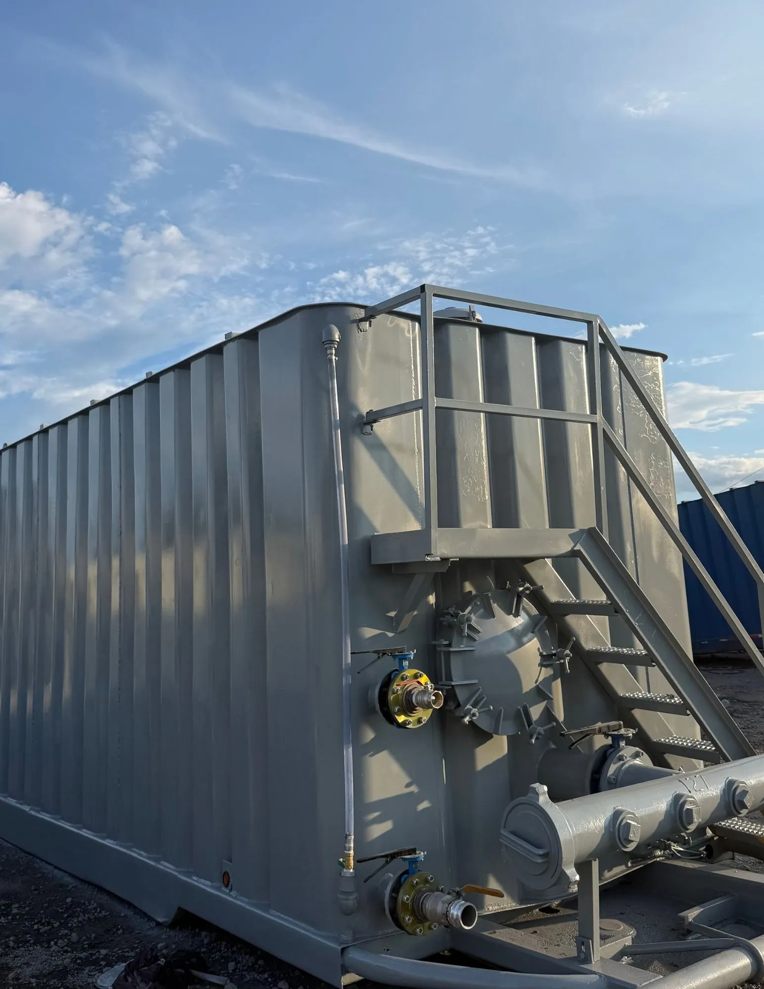 Acercamiento a frac tank con paredes corrugadas, escalera de acceso, válvulas con bridas y manifold de descarga