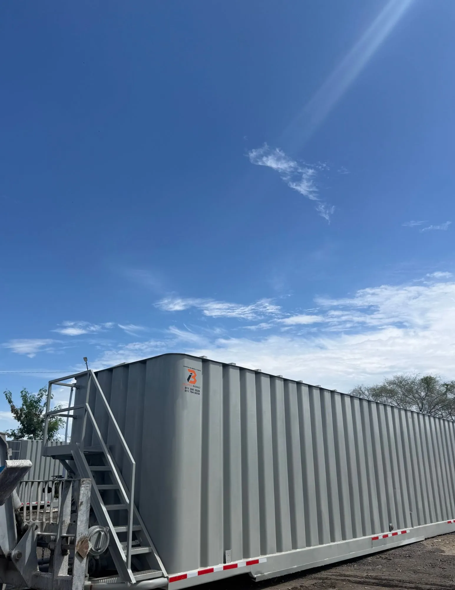 Frac tank gris con escalera, registro de hombre, válvula de mariposa y manifold de descarga en patio de equipos 2