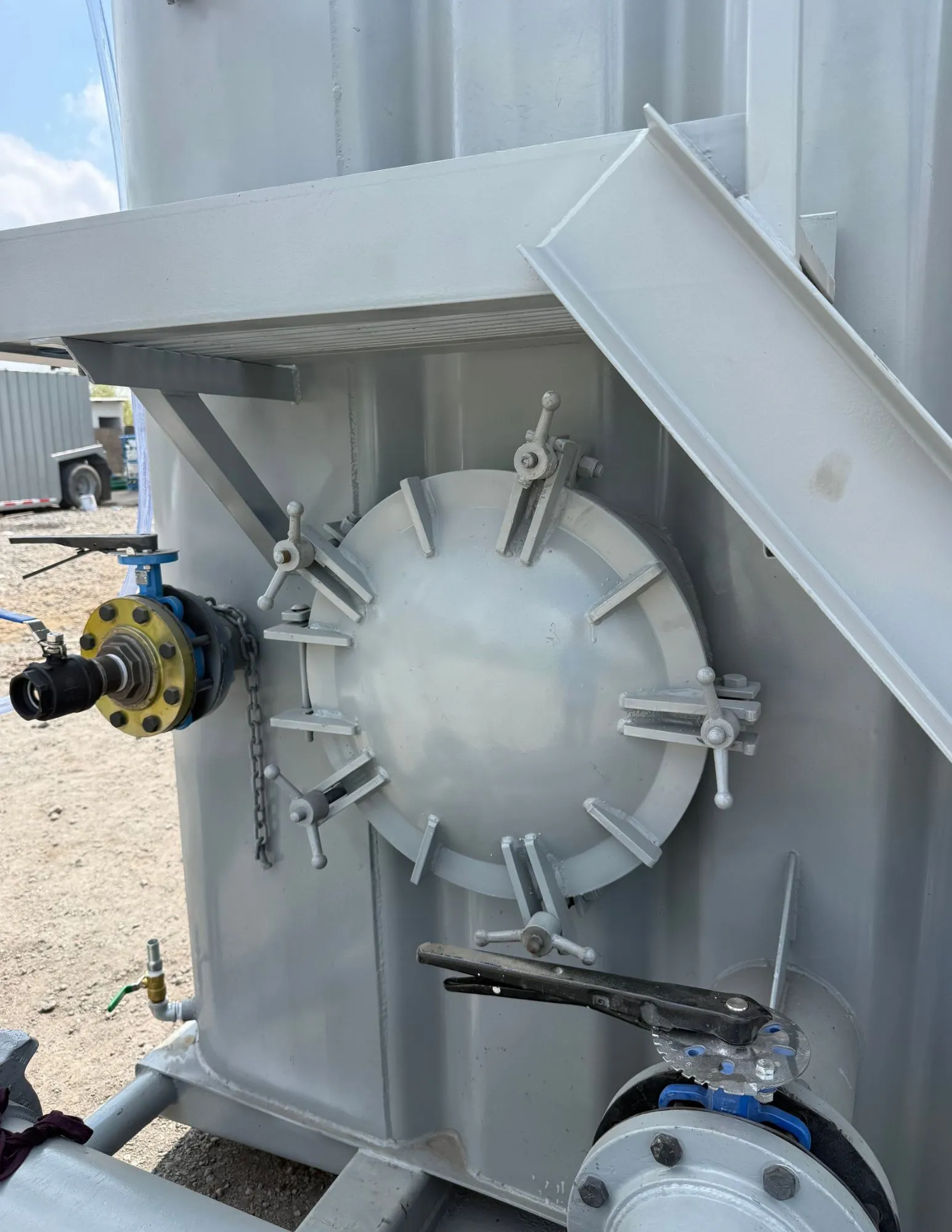 Frac tank gris con escalera, registro de hombre, válvula de mariposa y manifold de descarga en patio de equipos 5