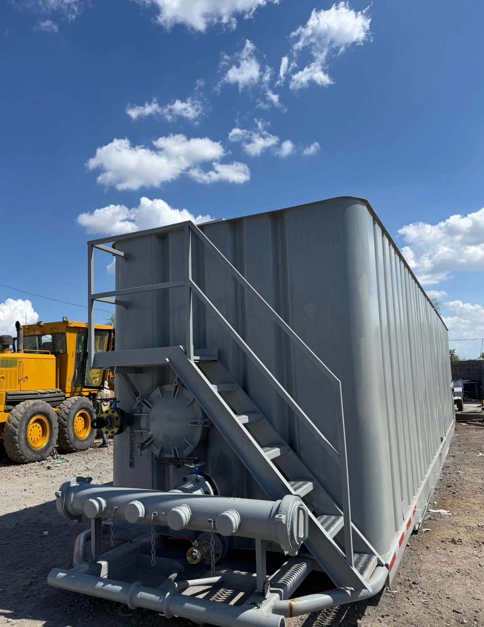 Frac tank gris con escalera, registro de hombre, válvula de mariposa y manifold de descarga en patio de equipos 6