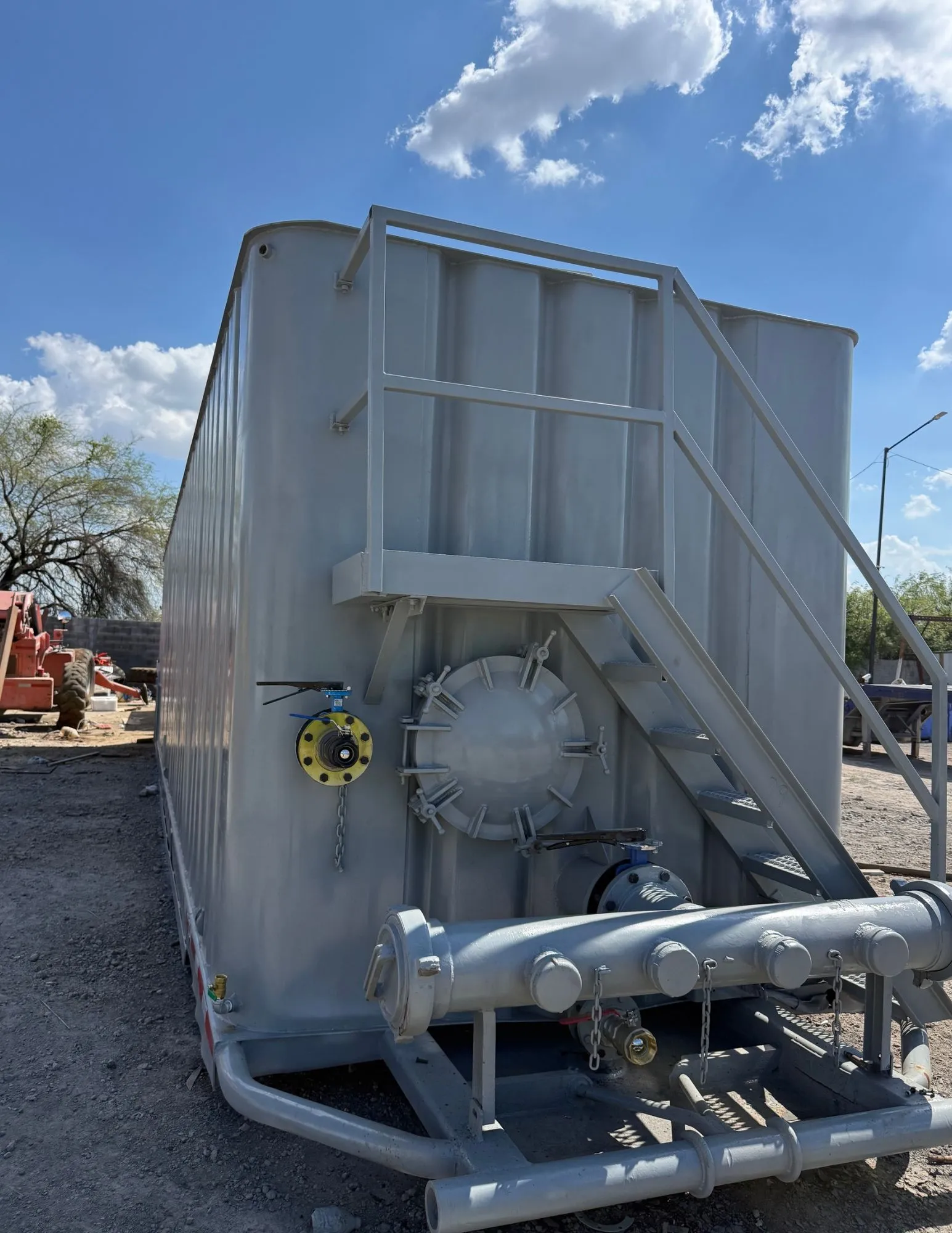 Frac tank gris con escalera, registro de hombre, válvula de mariposa y manifold de descarga en patio de equipos 7