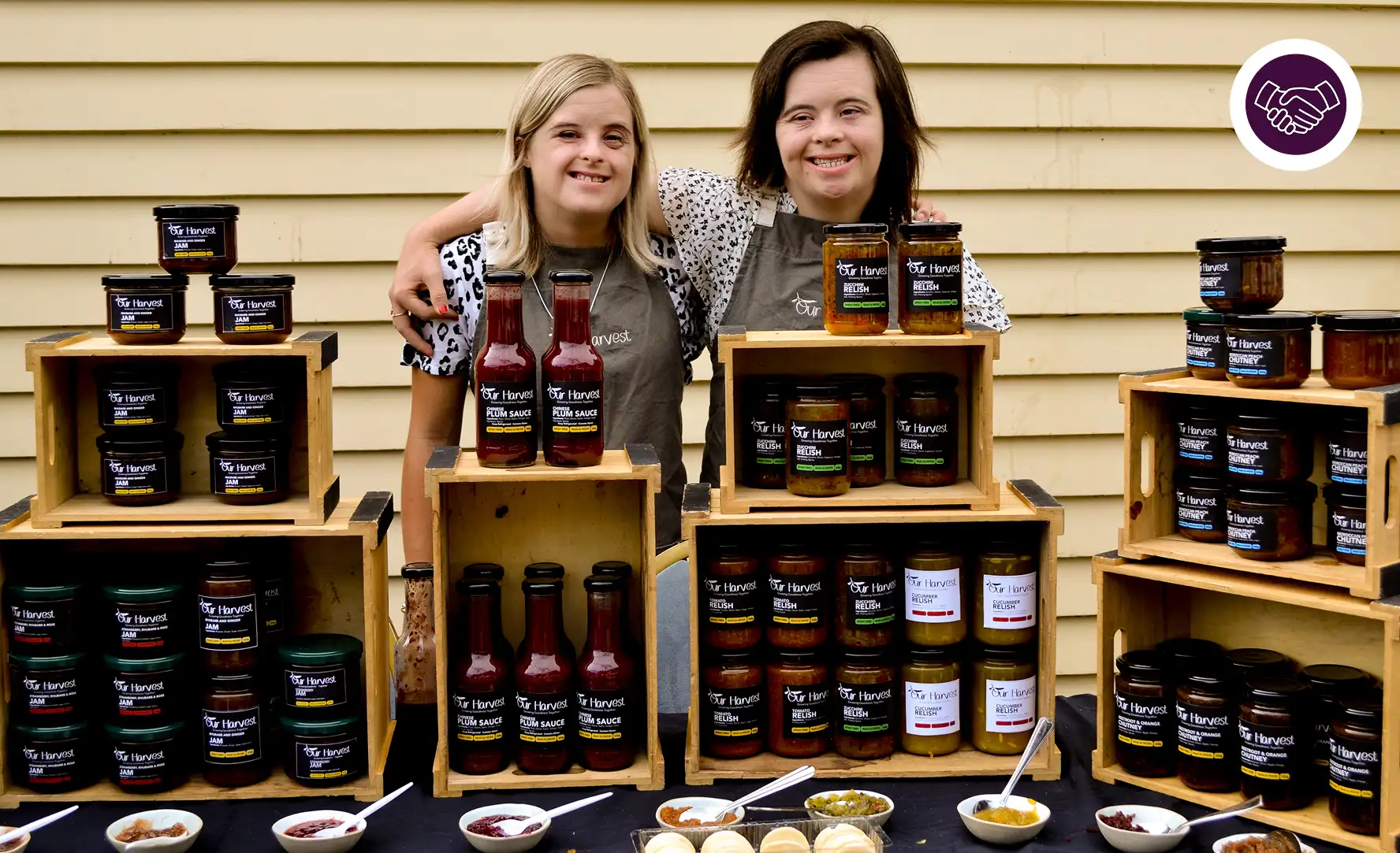 Two participants are pictured with their arms around each other smiling. The pair are standing behind various food products made with RecreateNZ.