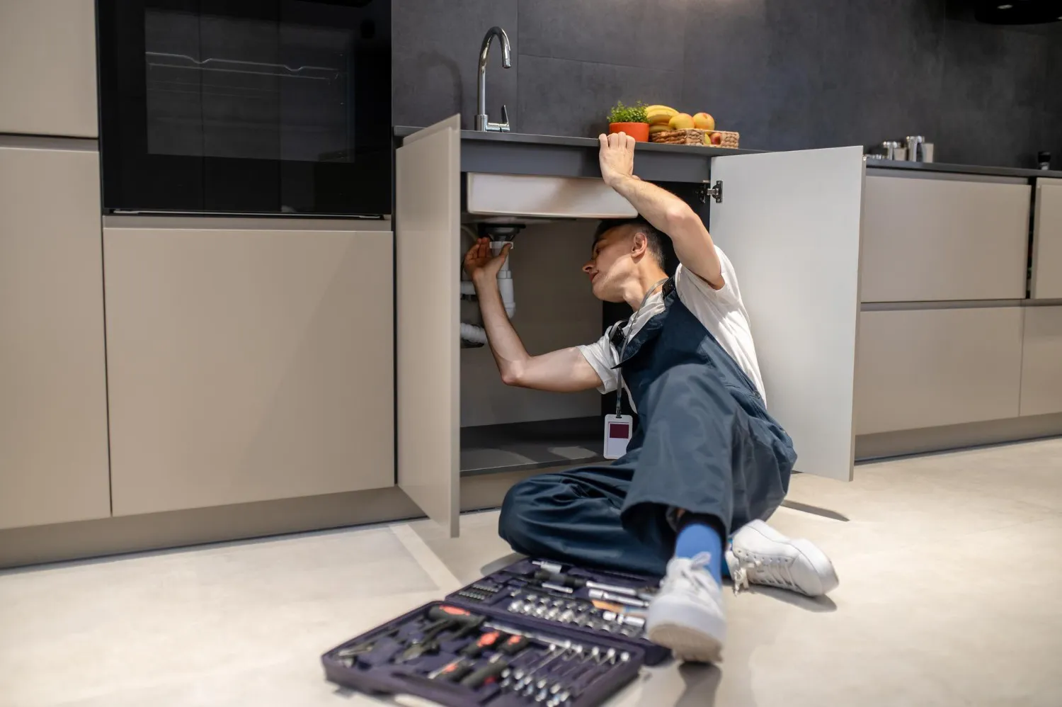 Image of a man working on kitchen plumbing
