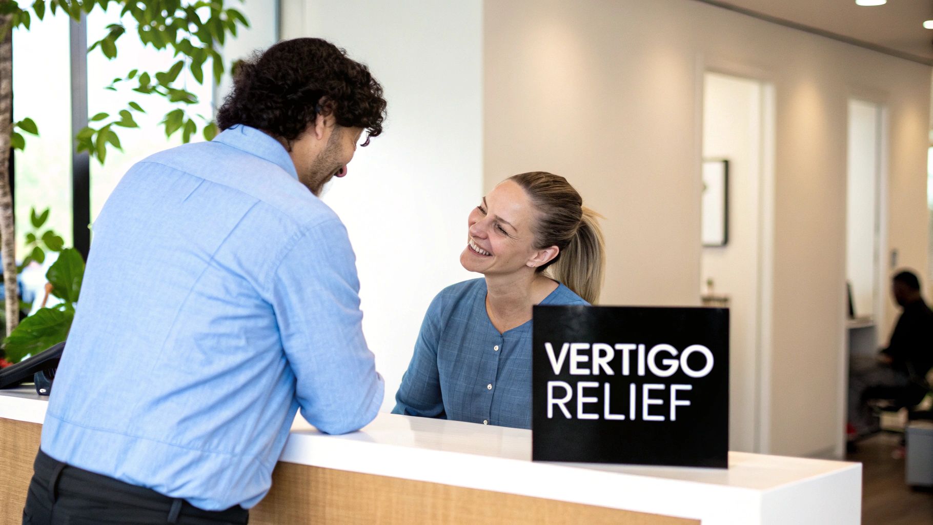 A man talks to a smiling woman at a clinic reception desk with a 'Vertigo Relief' sign.