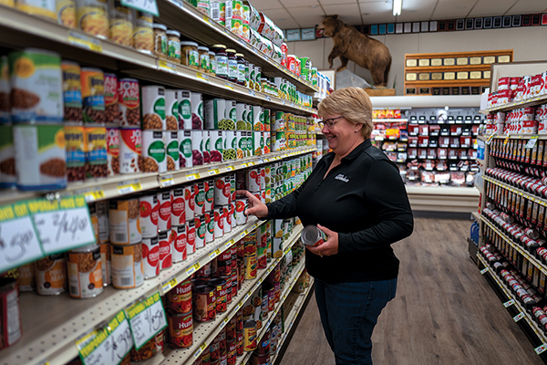 A woman holding an item in a aisle at a grocery store.