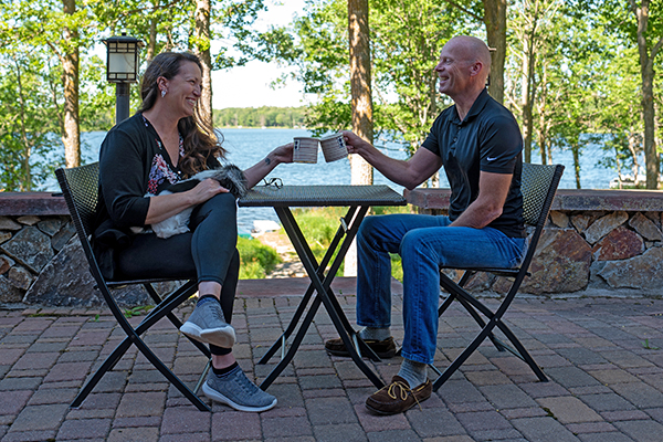 A man and woman sitting at a table on a patio by a lake.