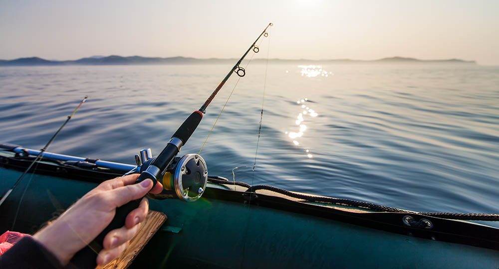 Person holding a fishing rod in a boat, with a clear, still body of water.