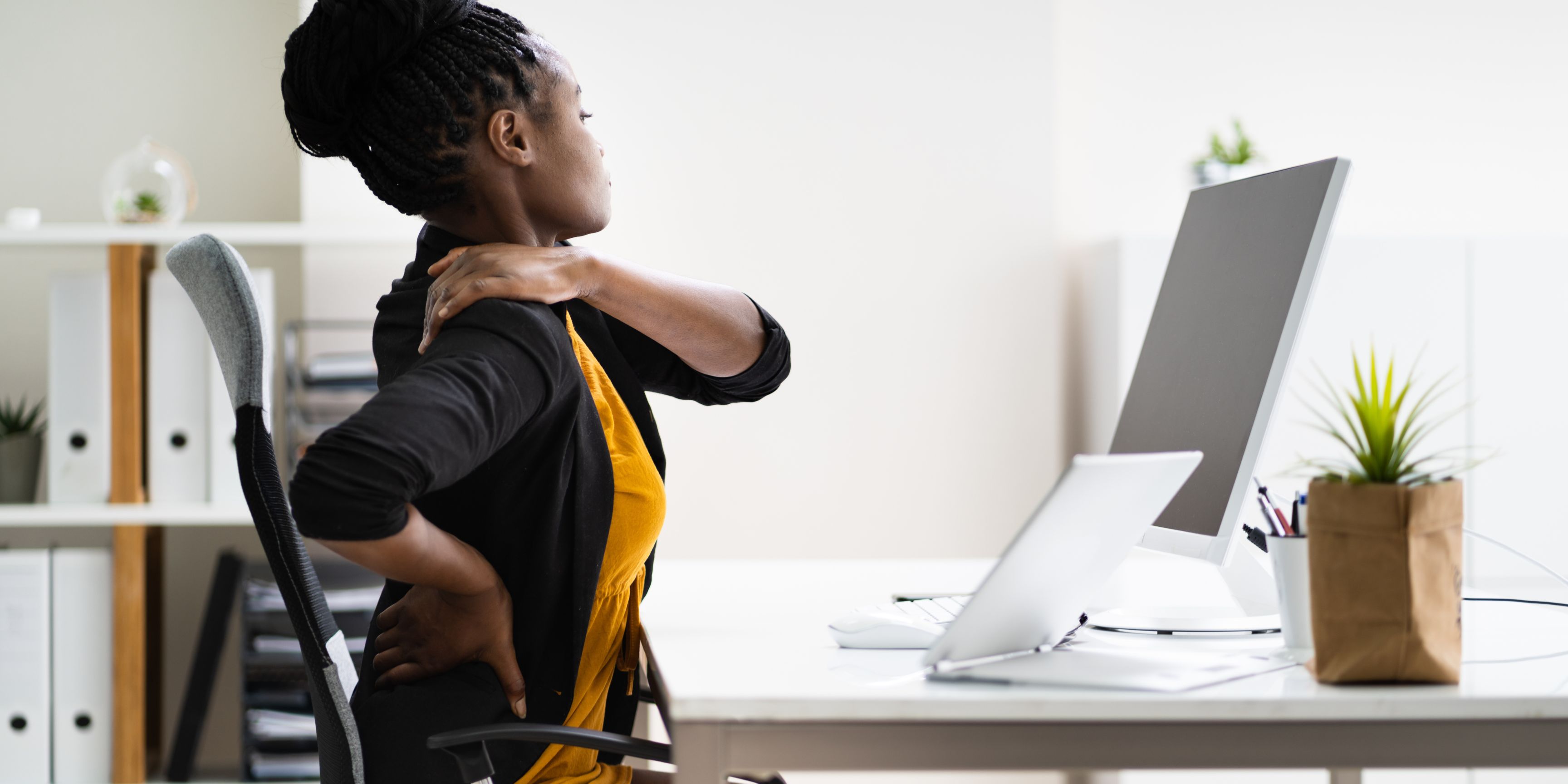 Femme à son poste de travail se touchant l'épaule avec inconfort