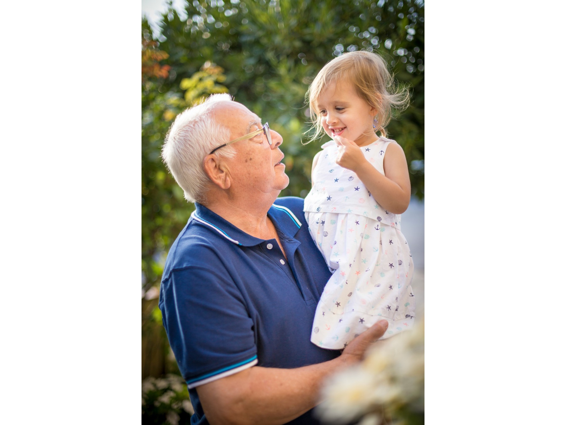 Smiling grandfather holding his young granddaughter outdoors, sharing a happy moment together.