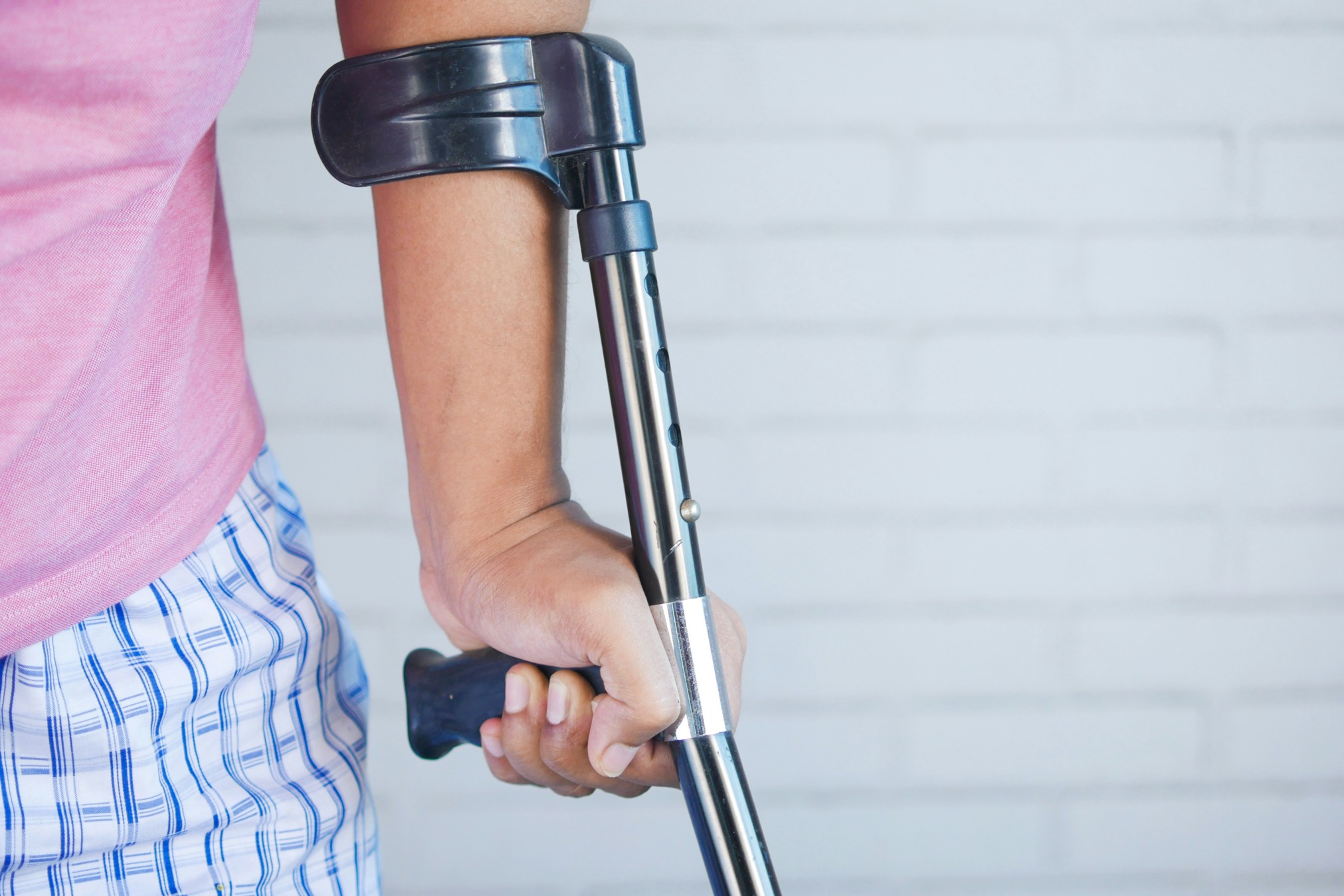 Close-up of a person holding a crutch, highlighting mobility challenges.