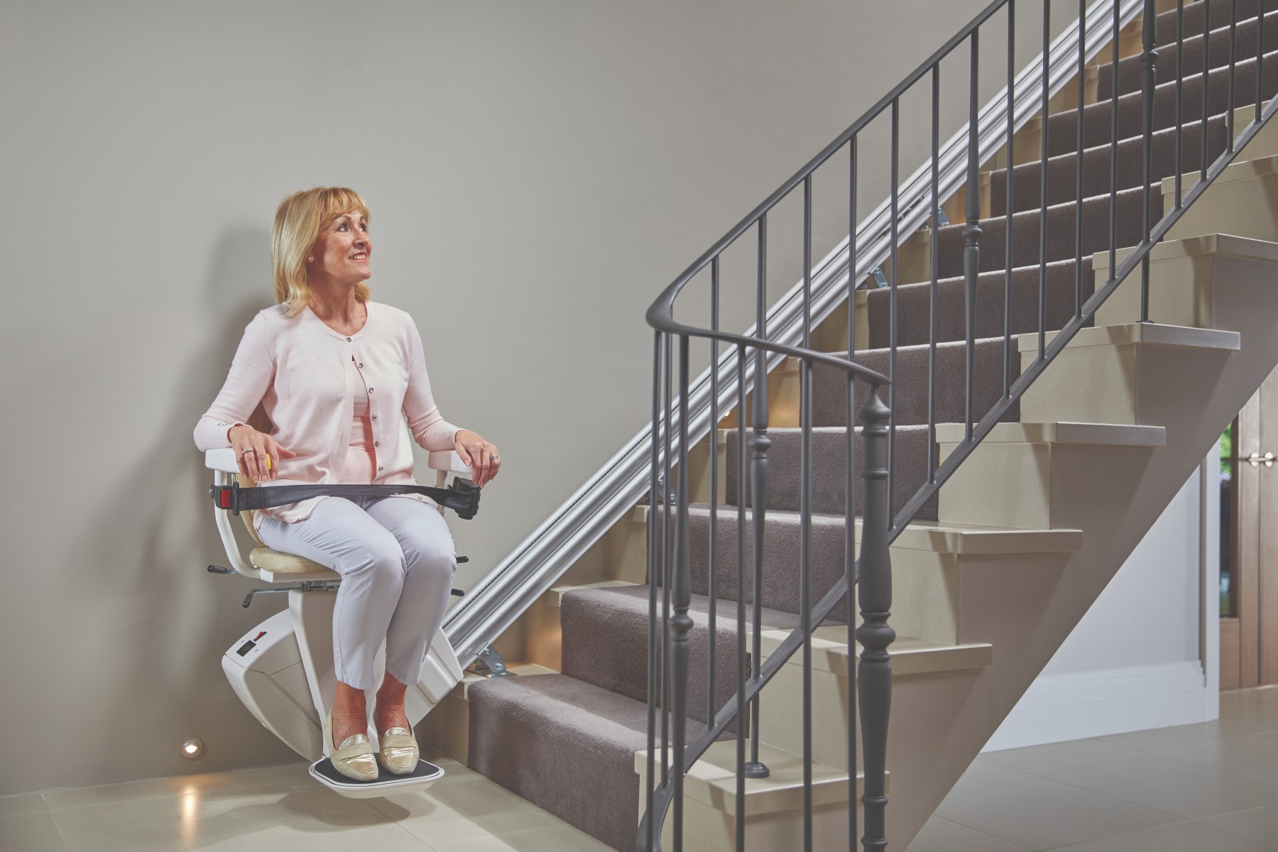 Couple at home using a stairlift on a straight staircase, showing remote control features and comfortable seated travel.