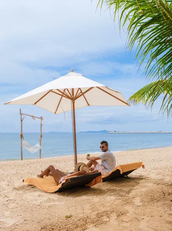 Two people relaxing under a beach umbrella by the ocean on a sunny day.