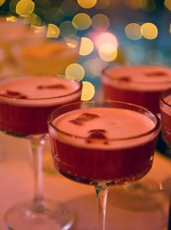Elegant cocktail glasses with pink foam and fruit garnish in a festive setting.