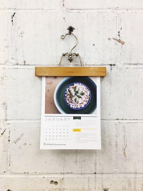 calendar held by a piece of wood and brass hanger hanging on a grungy painted white cinder block wall