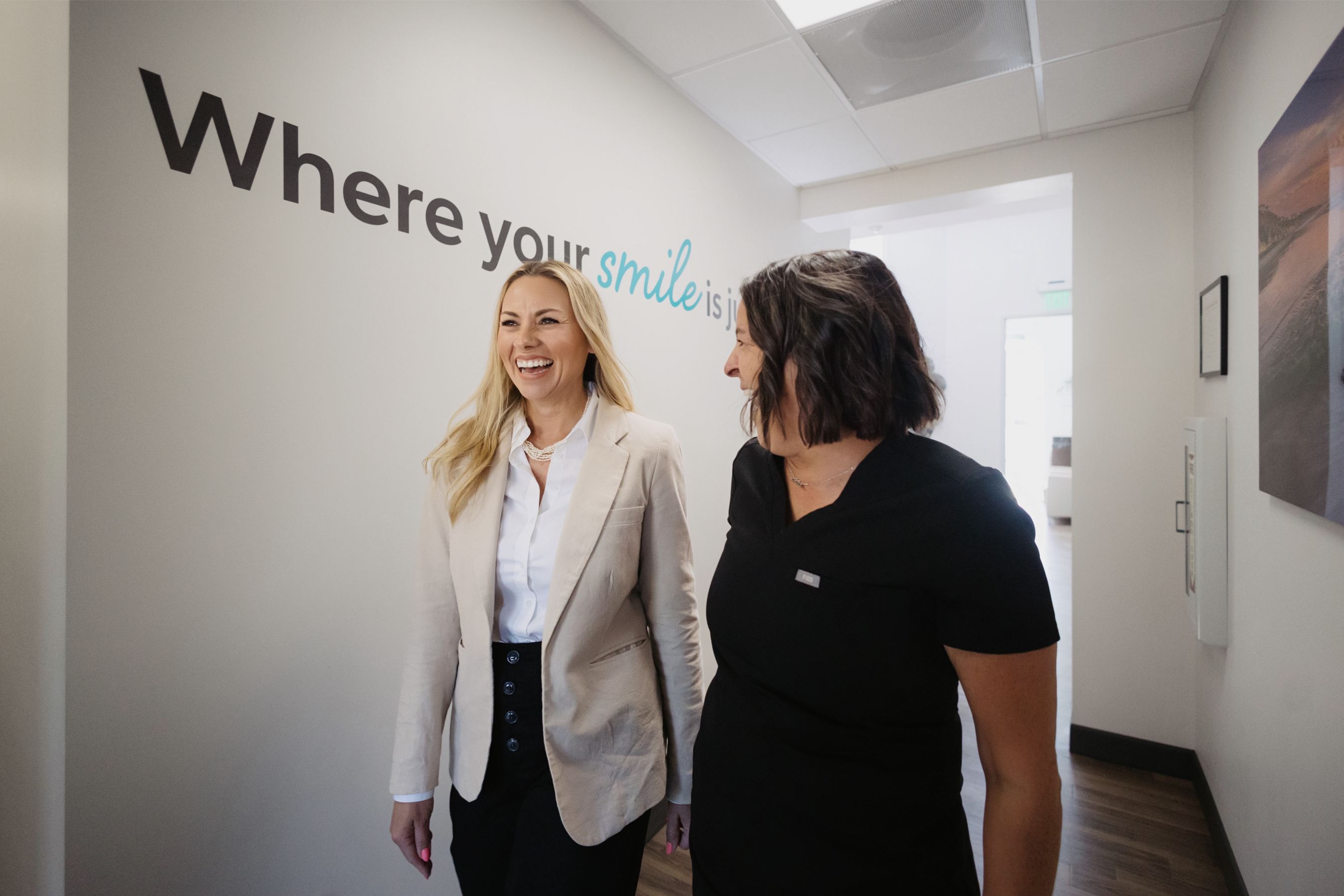 Two women smiling and walking down a hallway with the phrase 'Where your smile is' on the wall.