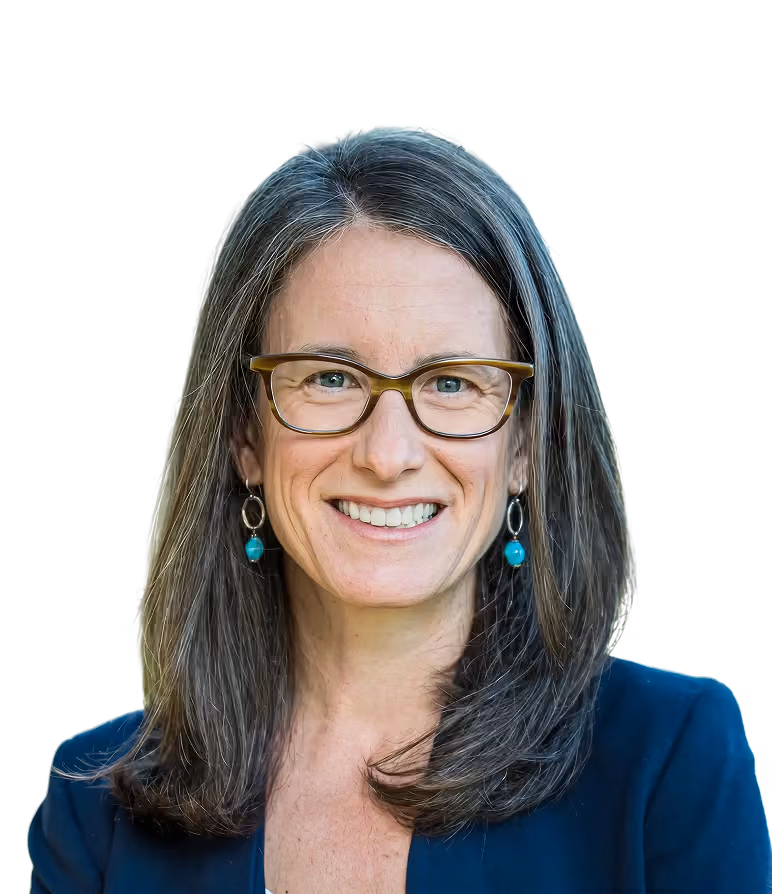 Smiling woman with shoulder-length gray hair, wearing glasses, turquoise earrings, and a dark blazer.