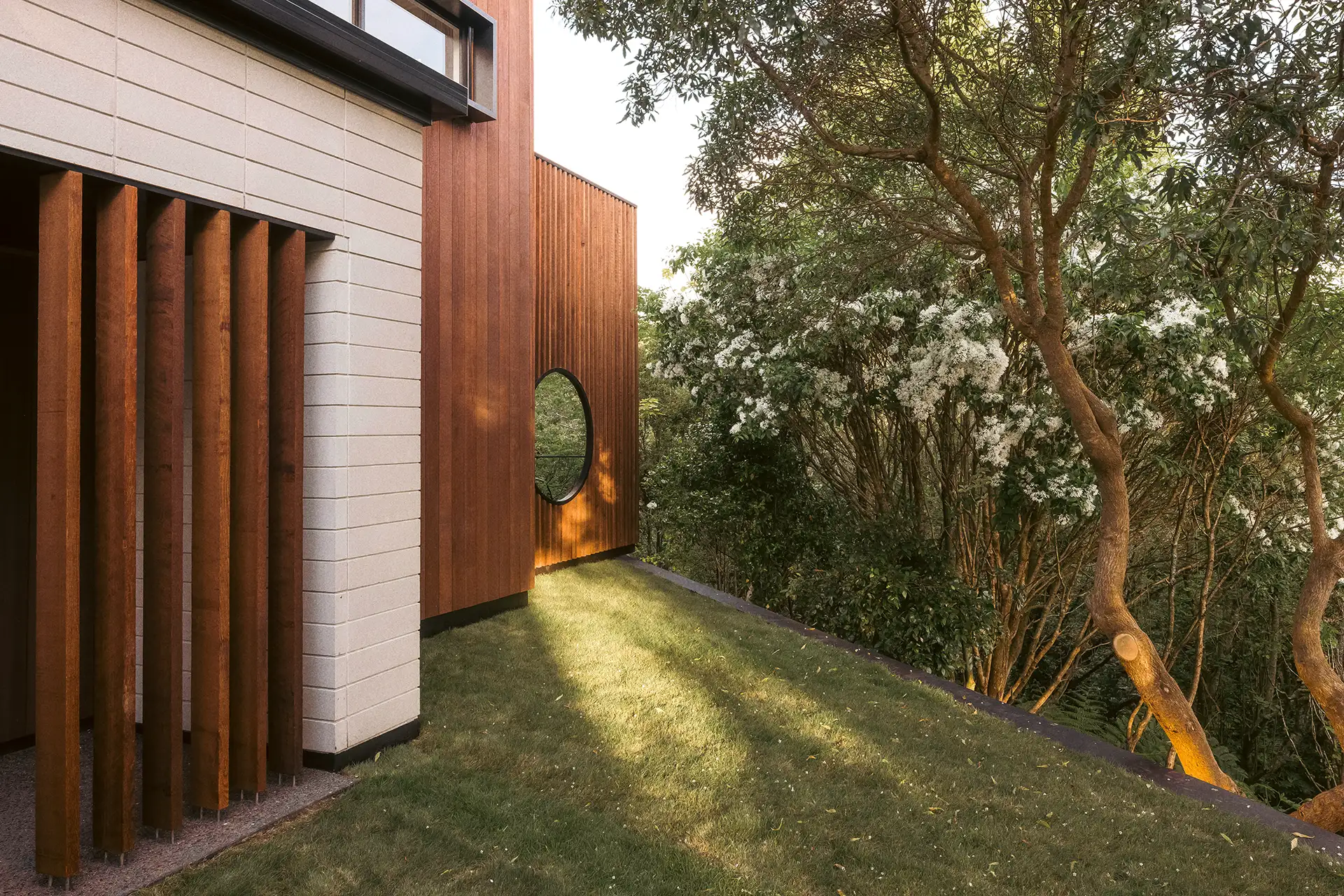 Close-up of an architecturally designed house featuring warm timber cladding, a circular window, and native garden backdrop.