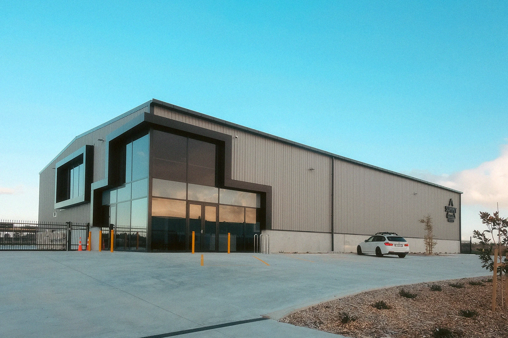 Modern industrial-style building with bold geometric lines and large glass windows, set against a bright blue sky.