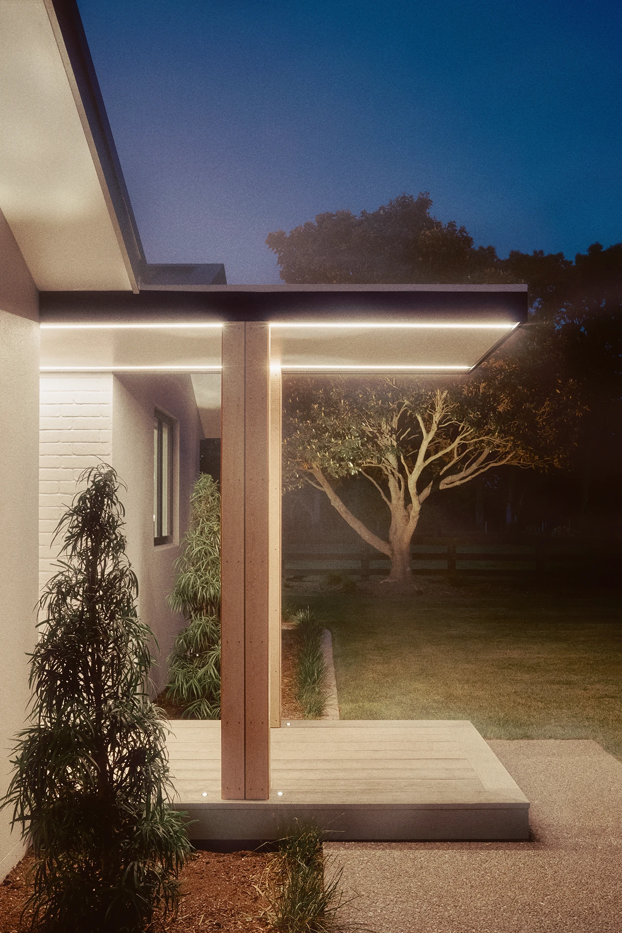 Evening view of contemporary residence with integrated LED lighting, timber details, and mature tree backdrop under twilight sky.
