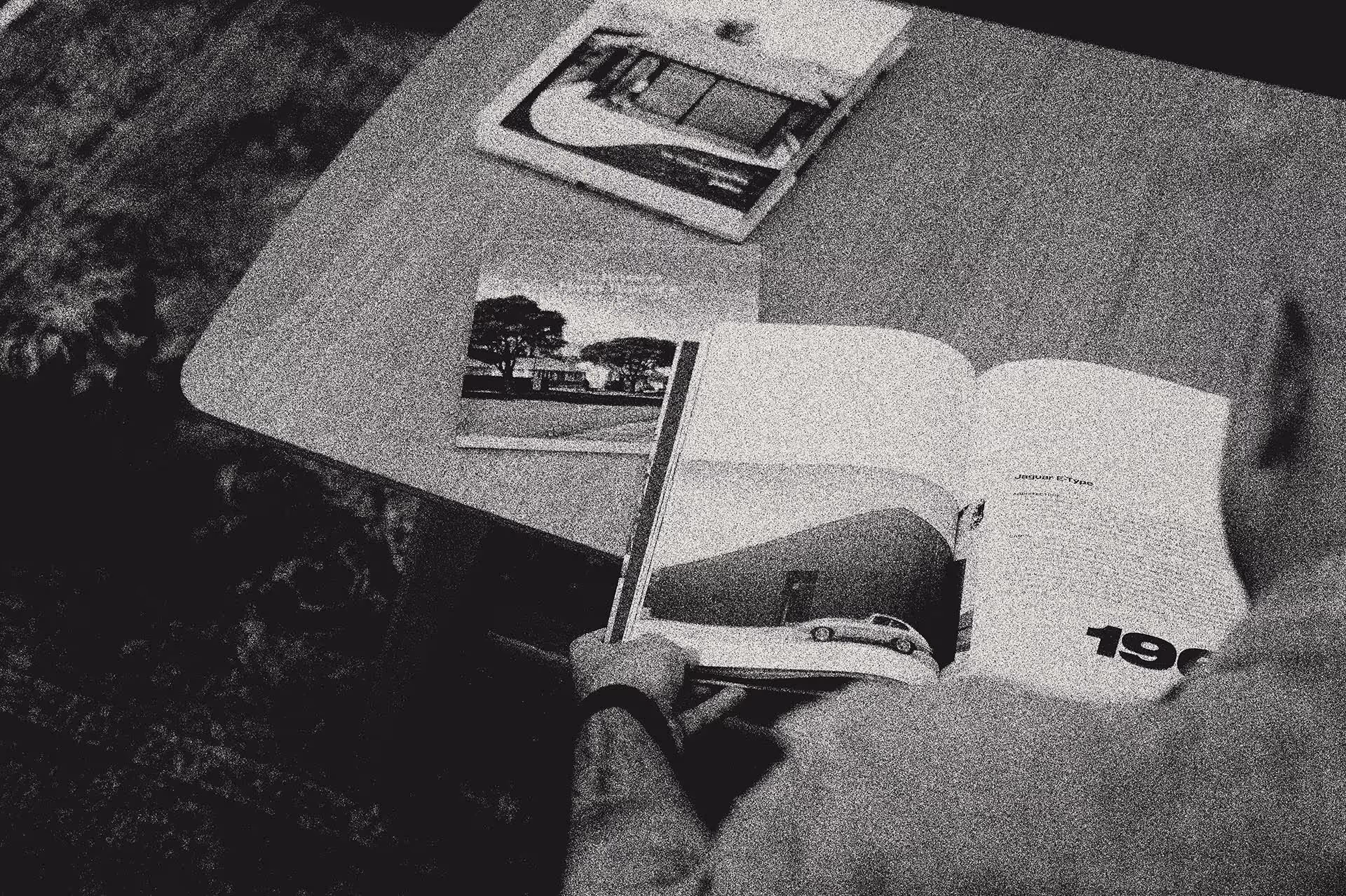Black and white overhead view of architectural drawings, reference images, and design materials spread across a workspace table.