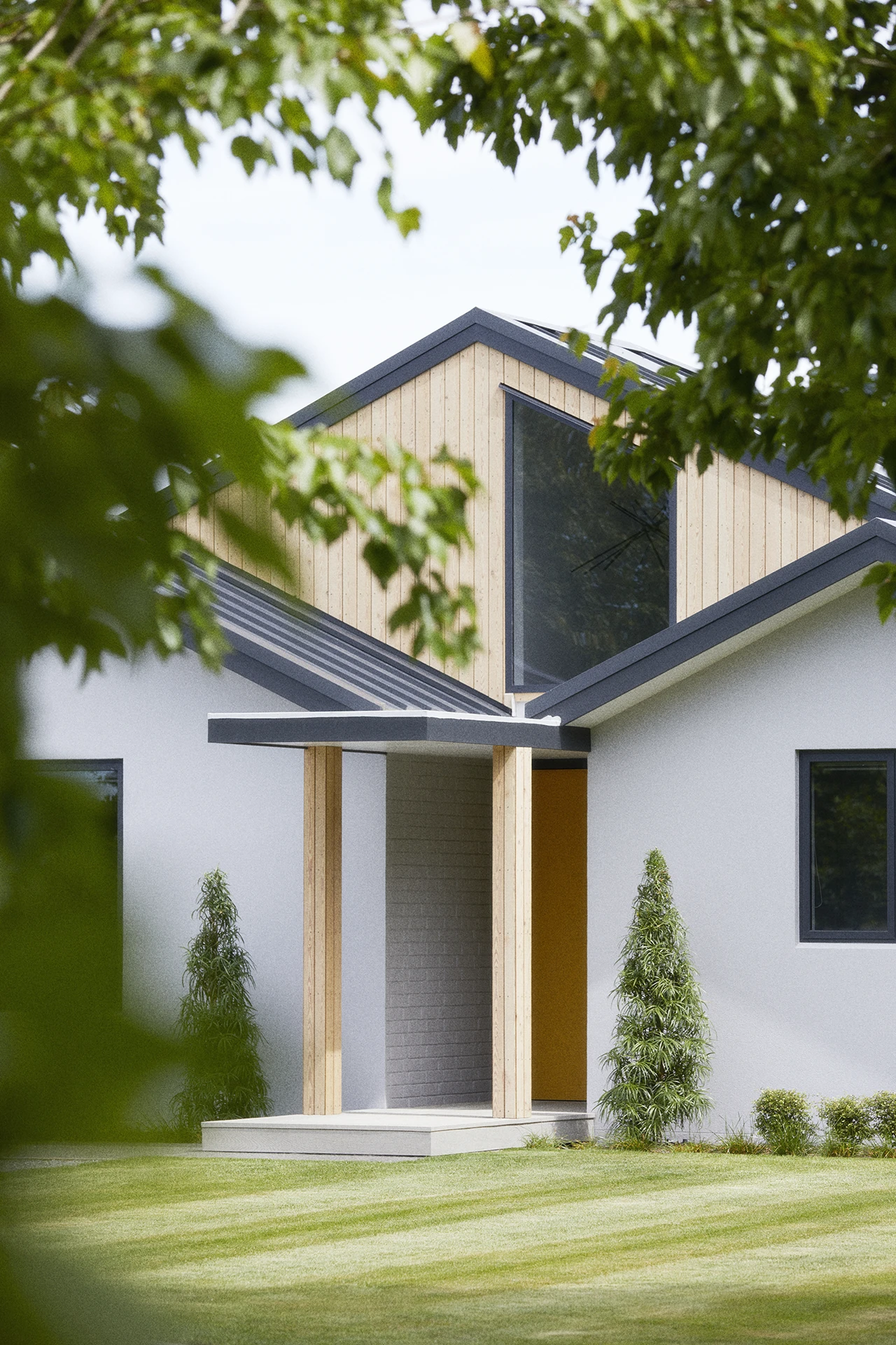 Modern home exterior showcasing timber upper level, white rendered walls, and covered entry with sculptural green landscaping.
