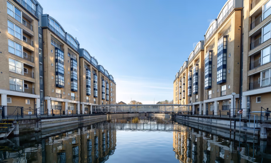 A high rise development with multiple buildings is photographed with two of the buildings overlooking each side of the Thames wharf. 