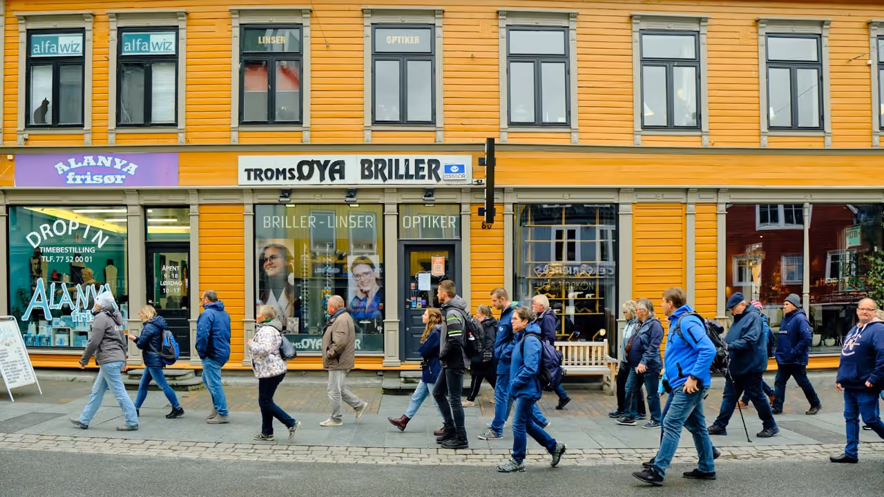 Group of pedestrians walking on sidewalk past yellow building with shops and large windows.