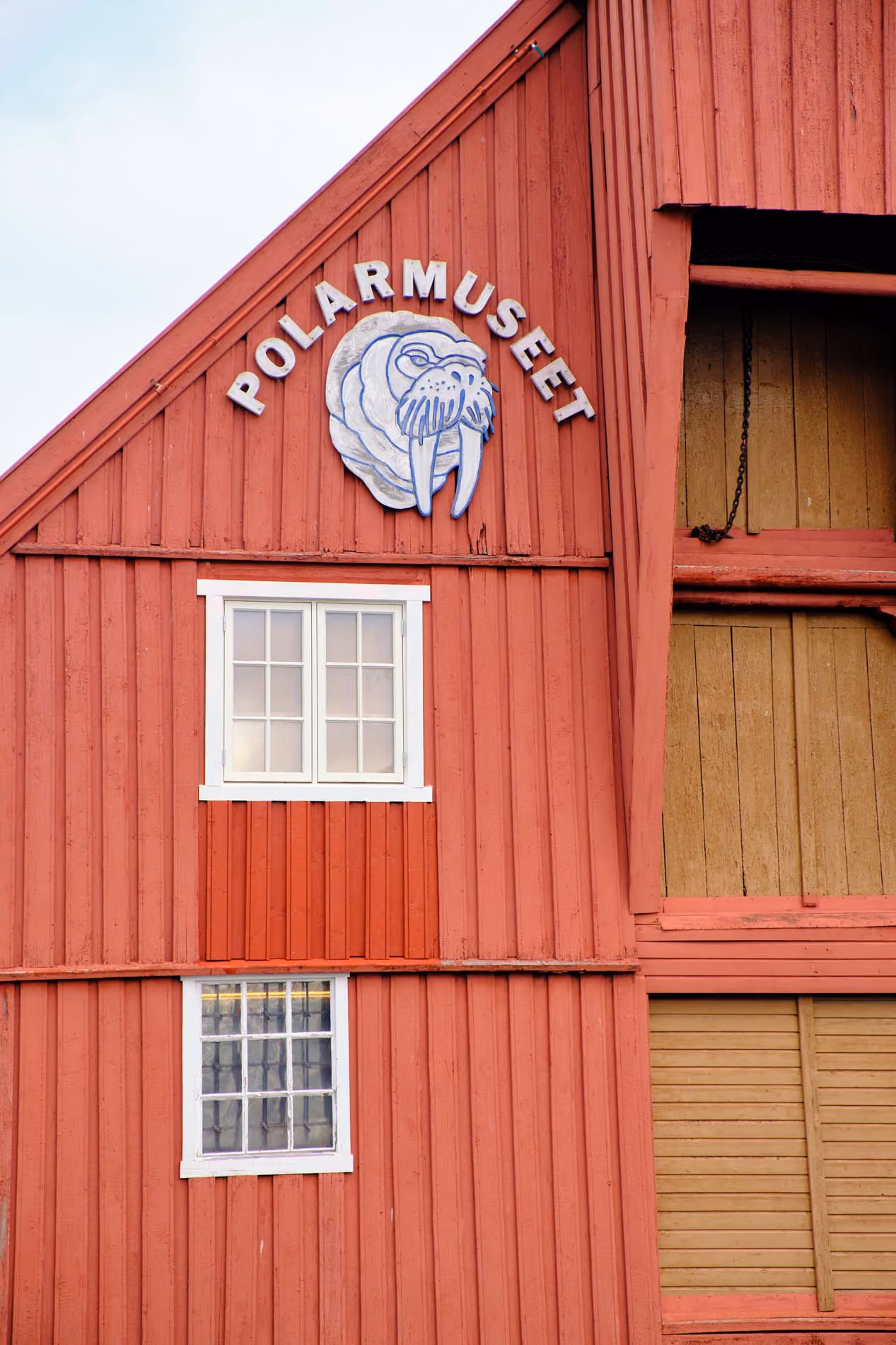 Red wooden building with two white-framed windows and a walrus head sculpture above the word 'POLARMUSEET' on the front facade.