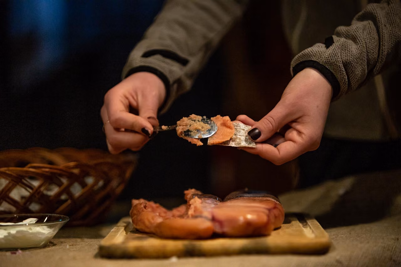 Person spreading fish roe paste onto a cracker, with sliced fish on a wooden board nearby.