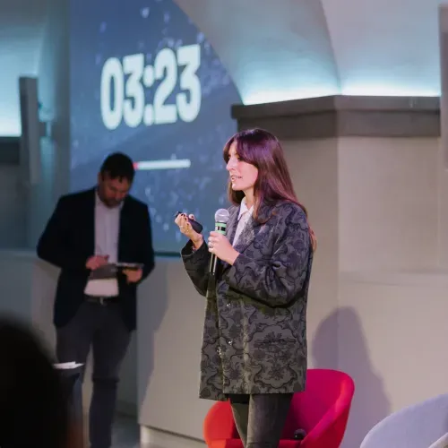 Ragazza che presenta un pitch su un palco durante un evento di startup, presso la sede dell'Innovation Center di Nana Bianca e FCRF a Firenze. L'evento è parte del programma di accelerazione Hubble, Cybershield, CTE Prisma, Italian Lifestyle, Bravo Innovation Hub ed Estra e-qube.